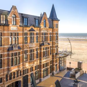 een groot bakstenen gebouw met het strand op de achtergrond bij Hotel Villa Select in De Panne