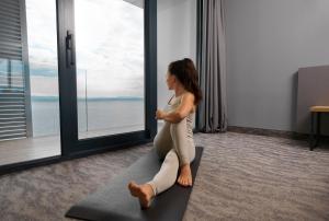 una donna seduta su un tappetino da yoga in una stanza con finestra di Hotel Istra - Liburnia a Opatija