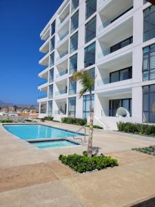 a apartment building with a swimming pool and a palm tree at Beachfront Luxury Seaside Condo + Pool & Jacuzzi in Rosarito