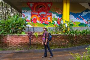 um homem parado em frente a uma parede com um mural em The Hosteller Wayanad em Vythiri