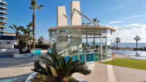 a large glass building with a swimming pool and the ocean at Apartament Sea Senses Summer in Punta Prima