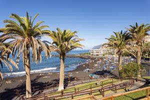 a beach with palm trees and a crowd of people at Playa La Arena with pool and privat parking in Puerto de Santiago