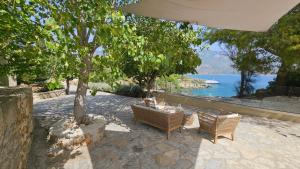 um pátio com duas cadeiras e uma árvore e água em Ploes Luxury Cottages em Cefalônia
