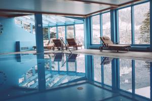 a room with a pool with chairs and windows at Alpine Spa Hotel Haus Hirt in Bad Gastein