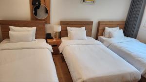 three beds in a room with white sheets and pillows at Heyy Seogwipo Hotel in Seogwipo