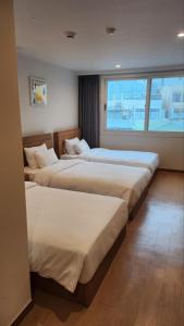 a hotel room with three beds and a window at Heyy Seogwipo Hotel in Seogwipo