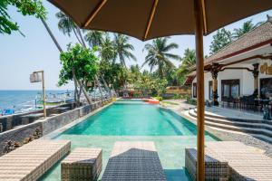 a swimming pool next to the ocean with an umbrella at Bali Taoka Beach Villa in Singaraja