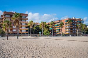a beach with palm trees in front of a building at AT049 Els Pins, primera línea de la playa con piscina y barbacoa in Torredembarra
