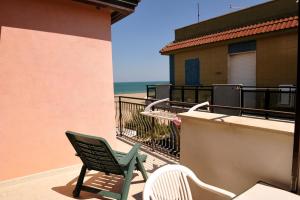 - un fauteuil vert et deux chaises sur un balcon avec vue sur la plage dans l'établissement La Perla delle Saline, à Margherita di Savoia