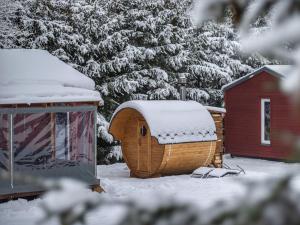 Ein hölzernes Hobbit-Haus im Schnee neben einem roten Schuppen in der Unterkunft Holiday Home Pod Liščím Kopcem 2-2 sauna by Interhome in Horní Branná + 14 Fotos