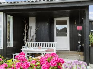 a white bench on the porch of a black house with pink flowers at Holiday Home Elisabeta - 60m from the sea in SE Jutland by Interhome in Juelsminde