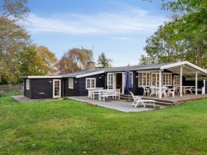 a black house with tables and chairs in a yard at Holiday Home Rami - 2km from the sea in Sealand by Interhome in Tisvildeleje