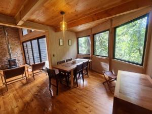comedor con mesa, sillas y ventanas en Mágica Casa Enclavada en el Corazón del Bosque, en Reserva Biológica Huilo Huilo