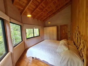 1 dormitorio con 1 cama en una cabaña con ventanas en Mágica Casa Enclavada en el Corazón del Bosque, en Reserva Biológica Huilo Huilo