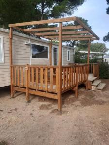 a wooden deck with a gazebo next to a house at Mobil-home cosy 166 in Narbonne