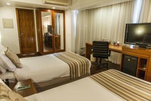 a hotel room with two beds and a desk and a television at Quality Porto Alegre in Porto Alegre
