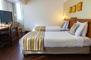 a hotel room with two beds and a desk and a television at Quality Porto Alegre in Porto Alegre