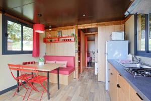 Huttopia Fontvieille في فونتفيل: مطبخ مع طاولة وكراسي حمراء في منزل صغير
