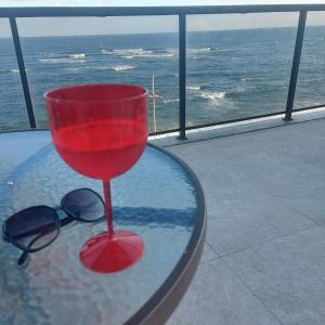 um copo vermelho sentado numa mesa de vidro com óculos de sol em Loft Pituba Sol em Salvador