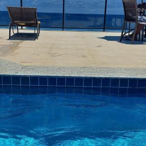 uma piscina com duas cadeiras sentadas ao lado em Loft Pituba Sol em Salvador