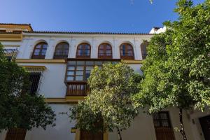 ein weißes Gebäude mit Fenstern und Bäumen davor in der Unterkunft Santa Cruz Refinadores Suite by Valcambre in Sevilla
