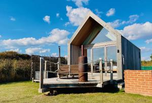 a small house with a bench on a deck at Lushna 12 Lux at Lee Wick Farm Cottages & Glamping in Clacton-on-Sea