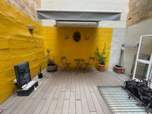 a patio with a table and chairs and a yellow wall at Valletta Collection - Merchant Str Apartment with large yard in Valletta