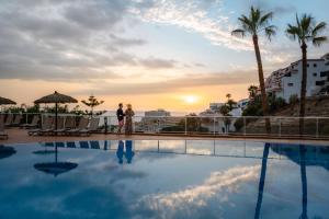 a couple standing next to a swimming pool at sunset at Wyndham Residences Costa Adeje in Adeje