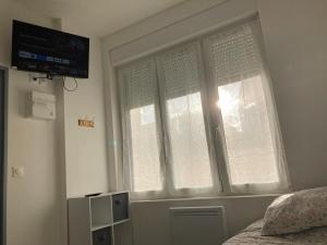 a bedroom with a window with white curtains and a television at Chez Aurel in Raismes