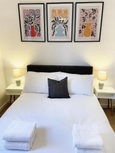 a bedroom with a white bed with three pictures on the wall at 3 bed home in Cheltenham Town Centre with FREE PARKING for 1 car in Cheltenham