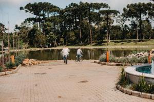 WoodStone Hotel Fazenda في غرامادو: شخصان يركبان الدراجات في حديقة بجوار بركة