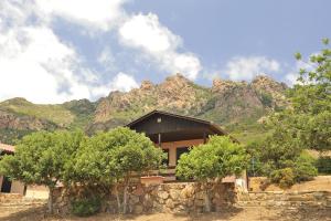 a house with a stone wall and mountains in the background at Villaggio Camping Tesonis Beach in Tertenìa