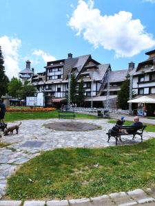 two people sitting on a bench in a park with a dog at Apartment Dunja Konaci in Kopaonik