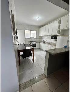 a kitchen with white cabinets and a desk and a table at AP Aconchegante a 60 Metros da Praia, vista mar 302 in Praia Grande