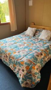 ein Bett mit einer bunten Decke darauf mit einem Fenster in der Unterkunft Cabañas parcela el ciprés in Melipeuco