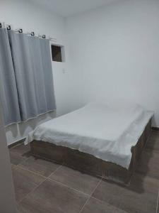 uma cama num quarto com lençóis brancos e cortinas em Casa em Unamar, Cabo Frio - com piscina privativa em Cabo Frio