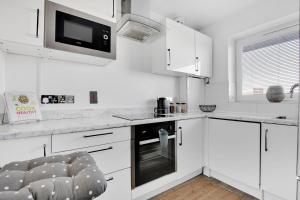 a white kitchen with white cabinets and a microwave at Peckham apartments by APS in London
