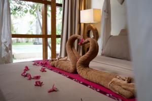 two towel swans sitting on a bed with pink rose petals at Villa Burung Gili Air Authentic 3-Bedroom Bamboo Villa with Private Pool in Gili Air