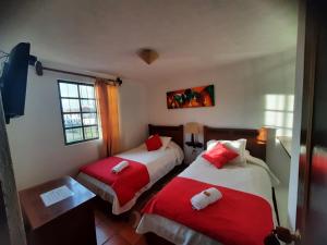 a bedroom with two beds with red and white sheets at Aparta Hotel El Refugio de María in Villa de Leyva