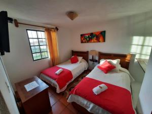 a bedroom with two beds with red and white sheets at Aparta Hotel El Refugio de María in Villa de Leyva