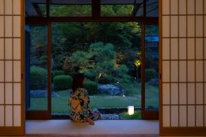 une femme qui regarde un jardin par une fenêtre dans l'établissement Tokiwa Bekkan, à Toyooka