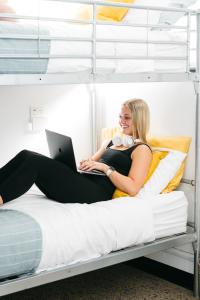 The Village Hostels Canberra في كانبرا: امرأة مستلقية على سرير بطابقين مع جهاز كمبيوتر محمول