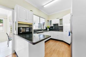 a kitchen with white cabinets and a black counter top at Archie s Abode By Coast Holidays in Patonga Beach