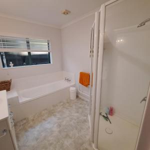 ein weißes Bad mit einer Badewanne und einer Dusche in der Unterkunft Hosts on the Coast - Rosberg Retreat in Mount Maunganui