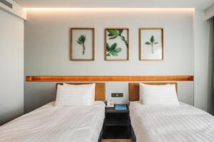 two beds in a room with three pictures on the wall at Hayata Hotel in Hengchun South Gate