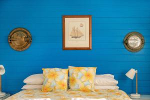a blue wall with a bed with pillows and a picture at A Perfect Stay - Beachcombers Cottage in Suffolk Park