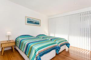 a white bedroom with a bed with a striped blanket at A Perfect Stay - Beachfront Tranquility in Suffolk Park