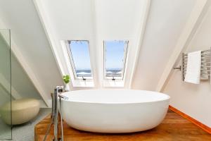 baño con bañera blanca grande y ventanas en Harbour House Hotel, en Hermanus