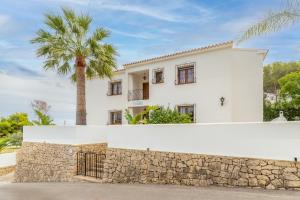a white house with a stone wall and a palm tree at La Boniquesa in Benissa