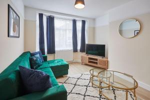 a living room with a green couch and a television at Elfleda Stay - Modern 5 bedroom house with parking in Cambridge